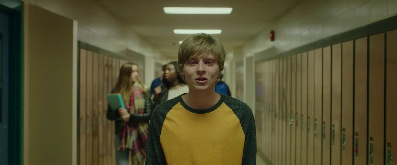 Spontaneous (2020) movie still: medium — A school hallway lined with numerous tan metal lockers illuminated by rectangular ceiling lights. A young…