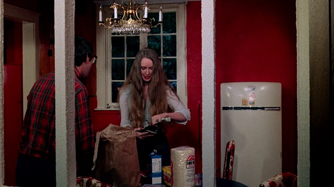 I Spit On Your Grave (1978) movie still: medium — A kitchen with vibrant red walls and a white-framed window above a table. A woman pulls items from…