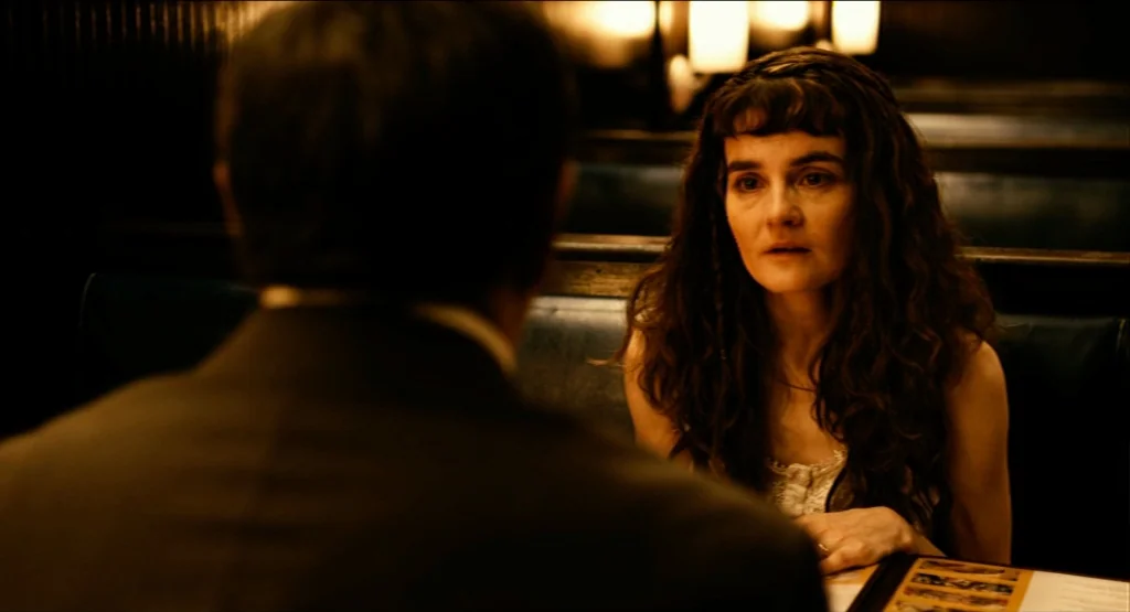 Life During Wartime (2009) movie still: medium — A dark, dimly lit booth interior features a woman sitting across from another person. The woman…