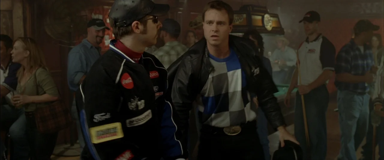 The Dukes of Hazzard (2005) movie still: medium — A crowded bar interior features dark wooden walls and patrons gathered in the background. Two men…
