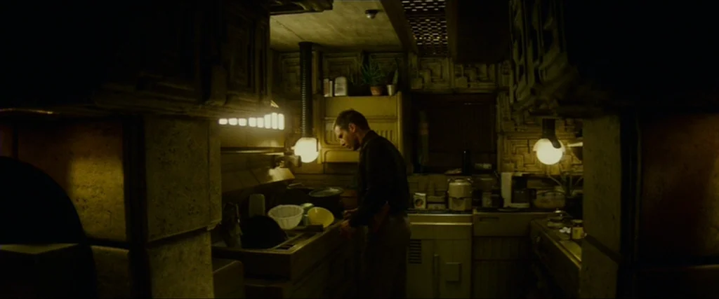 Blade Runner (1982) movie still: medium — A dimly lit, cramped apartment space features geometric wall textures and warm spherical lights. A man…