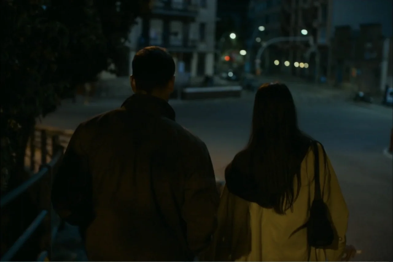 Cross the Line (2020) movie still: medium — An empty nighttime city street features blurred streetlights in the dark background. A man and a woman…