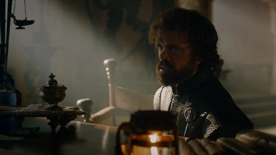 Game of Thrones (2017) movie still: medium — A dimly lit room features a cluttered desk with scrolls and a small metal vessel. A man sits at the…