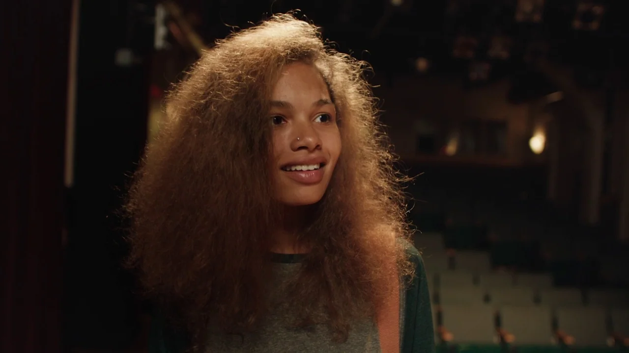 Madeline’s Madeline (2018) movie still: medium — A dark empty auditorium with rows of out-of-focus seats visible in the background. A young woman…