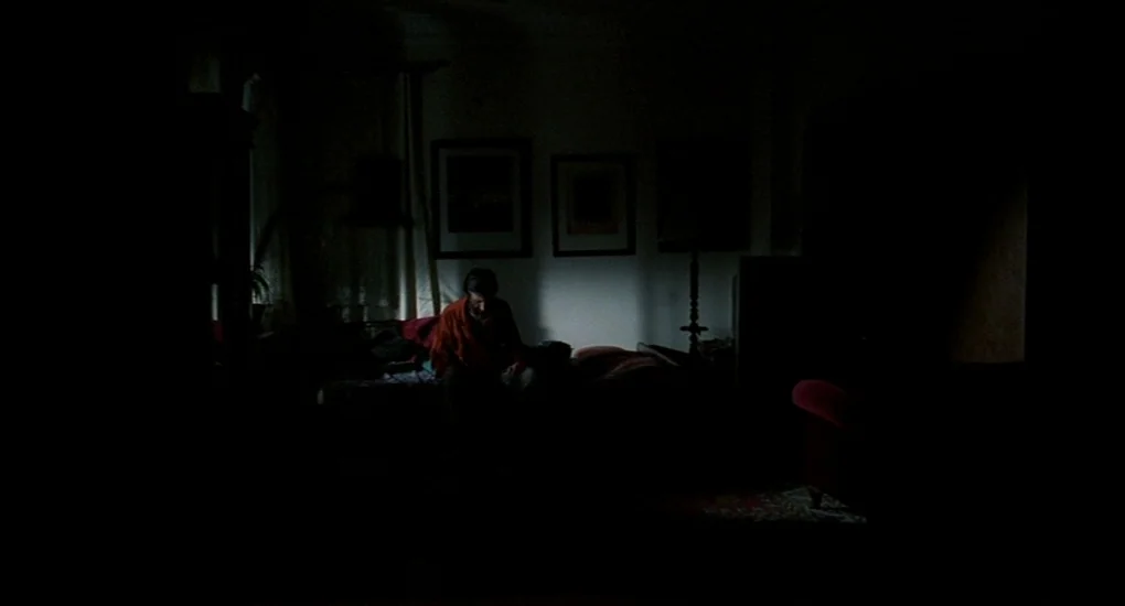 Uzak (2002) movie still: wide — A sparsely furnished room with a bed and wall art in near total darkness. A man sits alone on the side of the bed in…