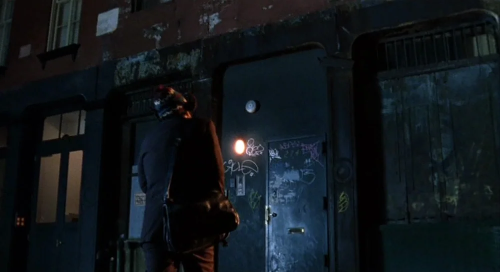 Hamlet (2000) movie still: fullbody — A dark brick apartment exterior at night features a metal door covered in graffiti. A lone man in a suit…