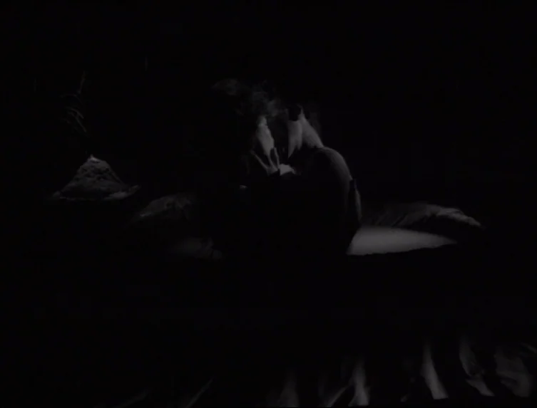 Eraserhead (1977) movie still: medium — A dark, minimally lit space with two individuals positioned close to each other. One person holds the other…
