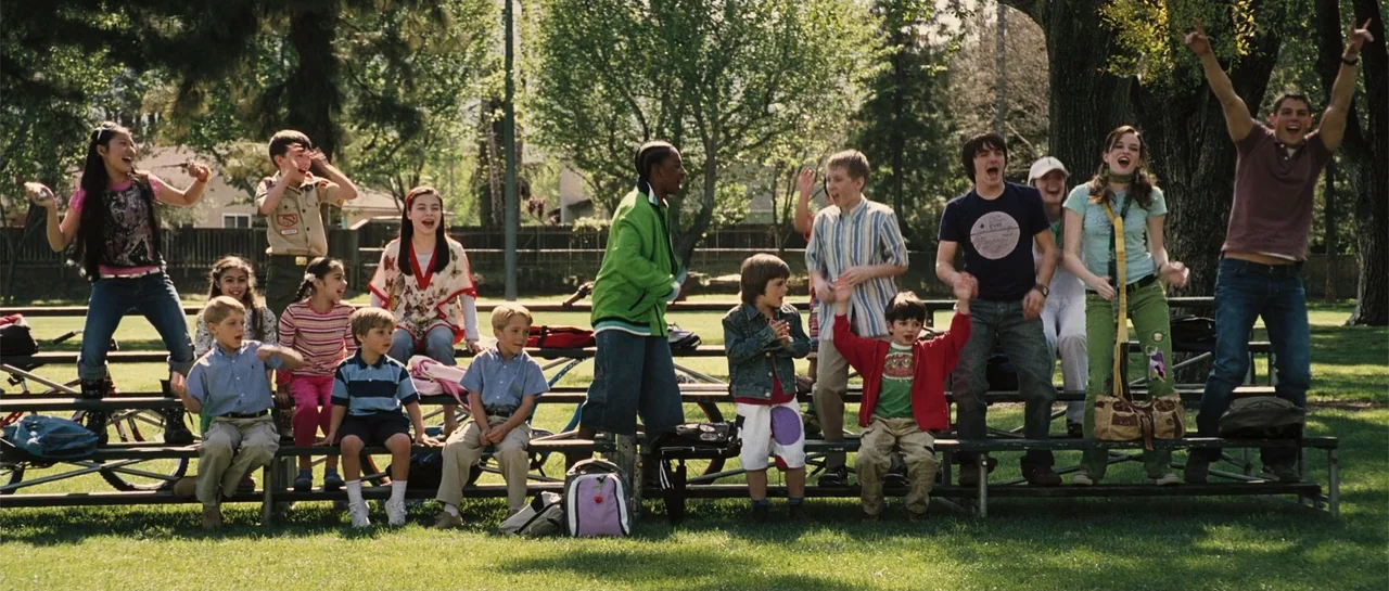 Yours, Mine & Ours (2005) movie still: wide — A sunny public park features metal bleachers filled with a large group of children. The group sits and…
