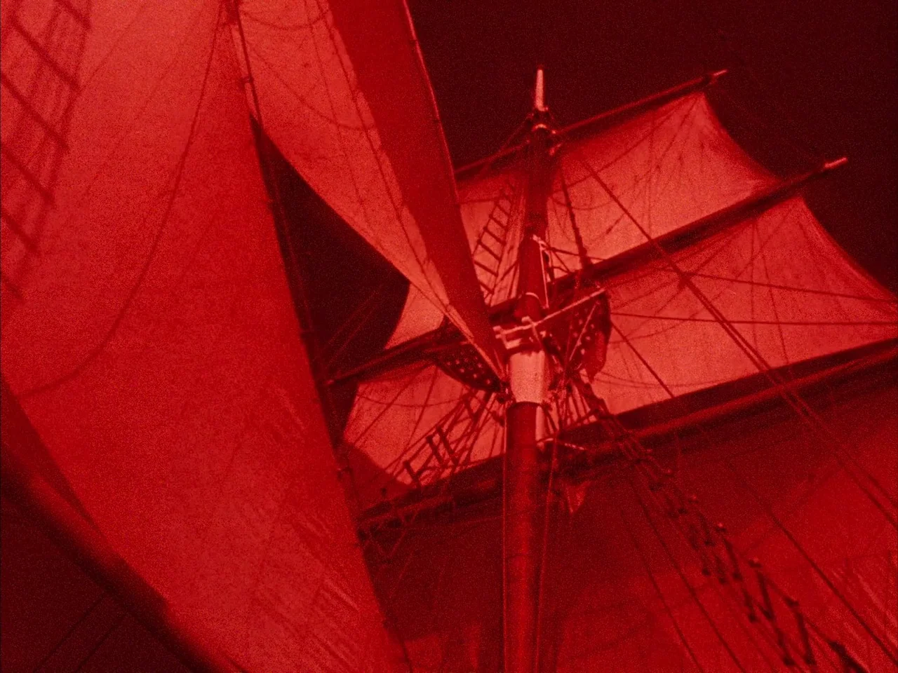 Dillinger is Dead (1969) movie still: establishing — A tall wooden sailing ship mast and canvas sails rise against a dark sky. The entire structure…