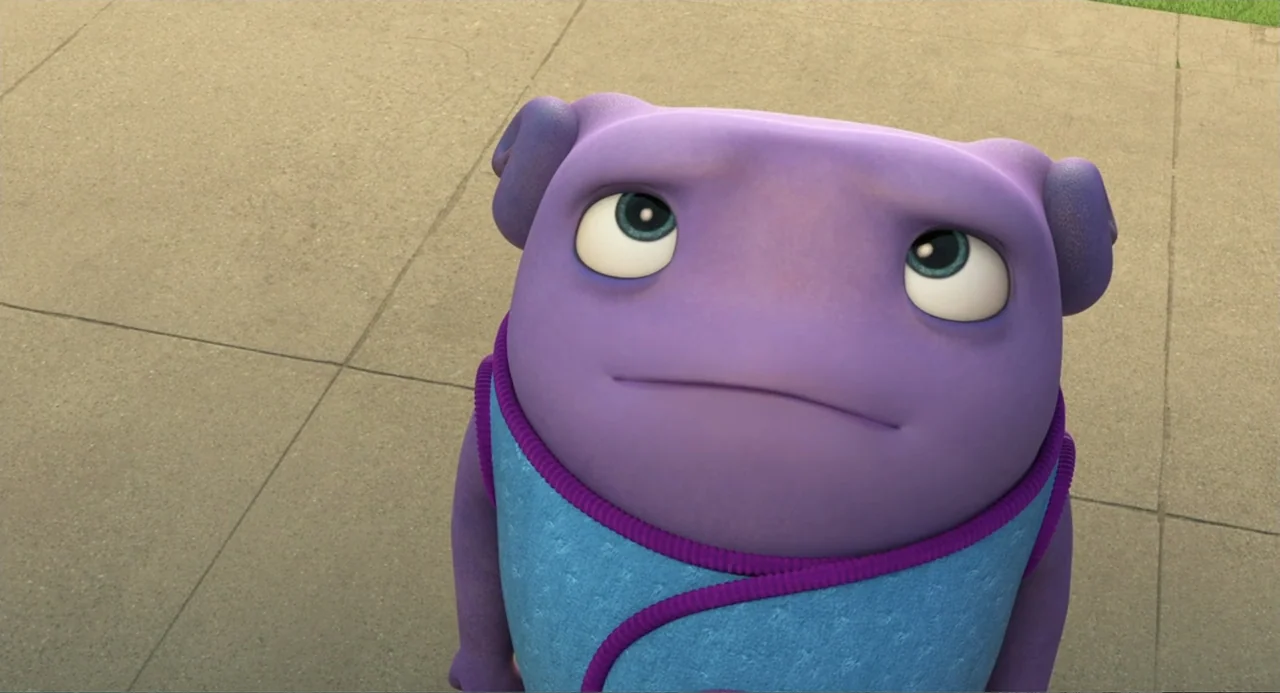 Home (2015) movie still: closeup — A light-colored concrete sidewalk viewed from a slightly elevated position. A purple alien character looks upward…
