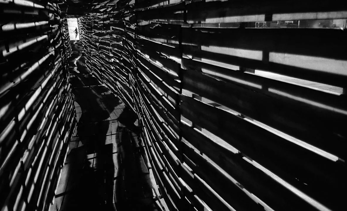 The Trial (1962) movie still: wide — A dark, narrow passageway is constructed from stacked horizontal wooden slats. A distant bright opening at the…