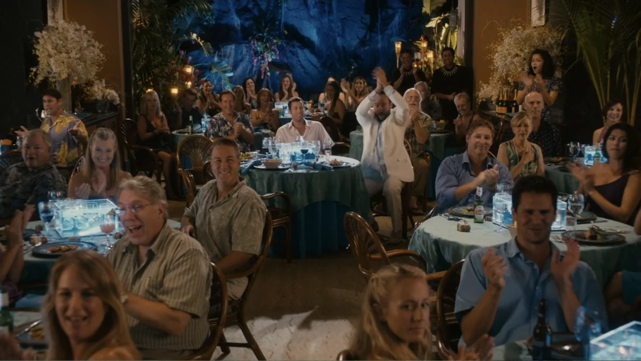 Just Go with It (2011) movie still: wide — A crowded restaurant dining room features round tables with light blue cloths and guests. People in…