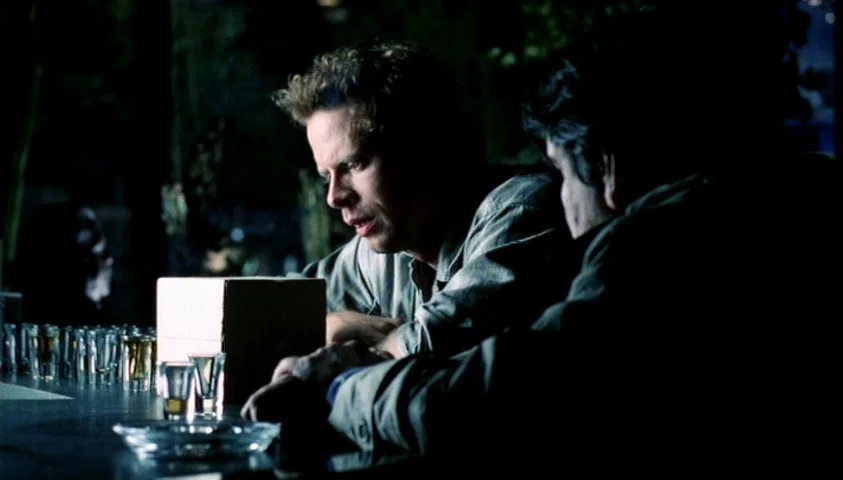 Maelström (2000) movie still: medium — A dimly lit bar setting with a dark counter and several empty glass tumblers. Two men in plain clothing lean…