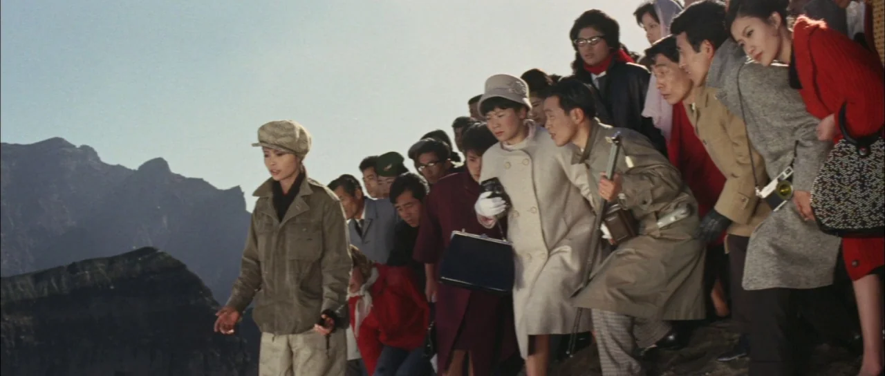 Ghidorah The Three Headed Monster (1964) movie still: wide — A group of people dressed in 1960s attire stand on a rocky mountainside. The crowd…
