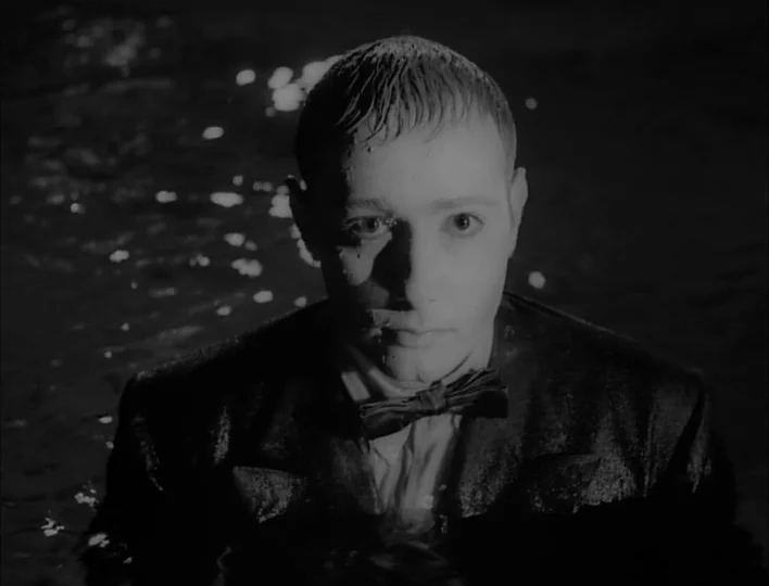 Carnival of Souls (1962) movie still: closeup — A man in a wet suit stands in dark water at night. He is submerged up to his chest while facing the…