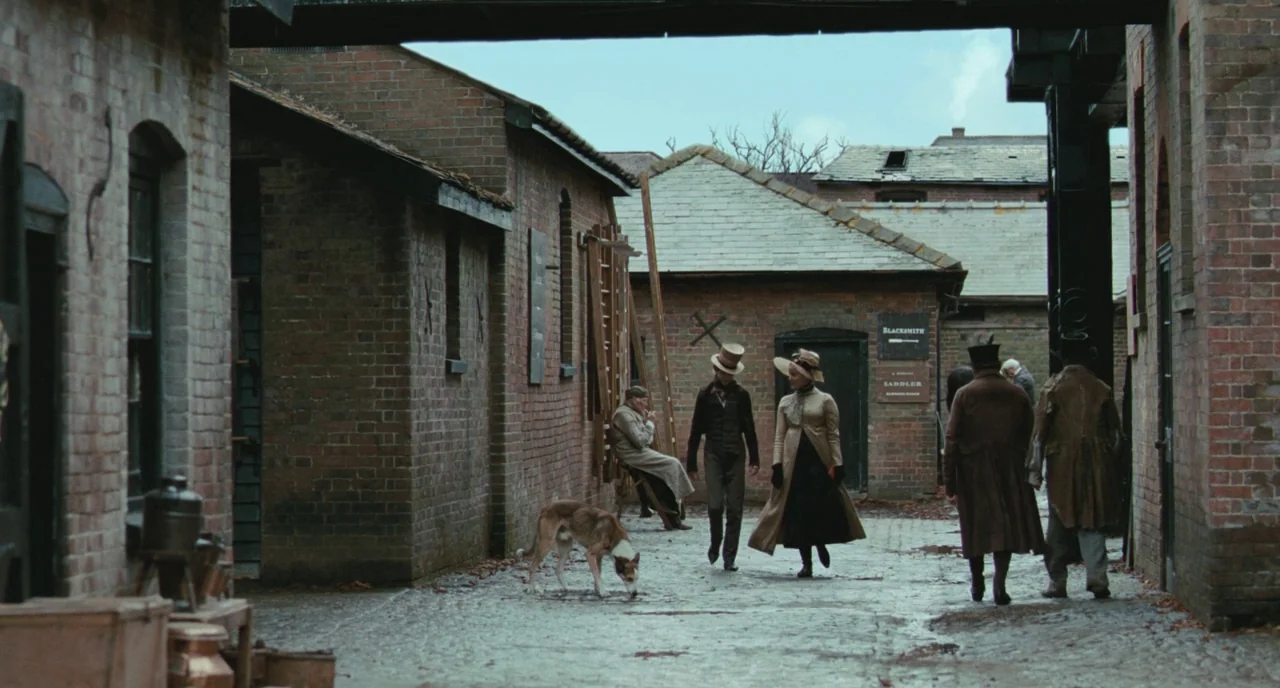 Bright Star (2009) movie still: fullbody — A 19th century industrial brick courtyard contains several low structures with slate roofs. A group of…