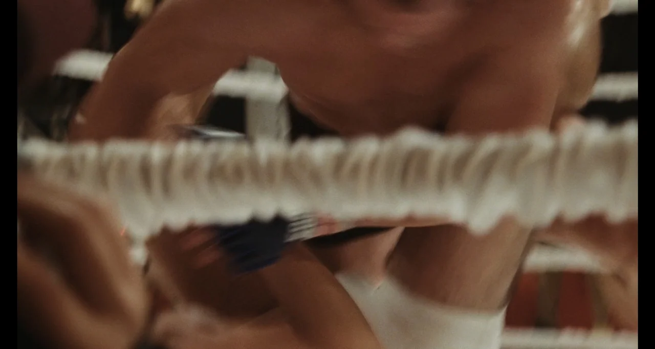 The Smashing Machine (2025) movie still: medium — A close view of a fighting arena shows the textured ropes of a ring. A shirtless male fighter in…