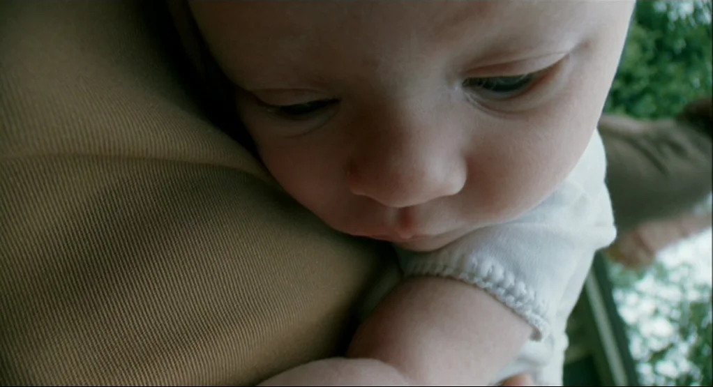 The Tree Of Life (2011) movie still: closeup — The frame shows a close-up of an infant resting on an adult's shoulder. Green foliage is visible in…