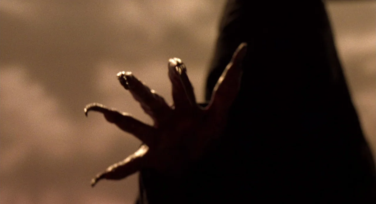 Tales from the Crypt: Demon Knight (1995) movie still: closeup — A dark, blurred space with a warm, hazy glow in the background. A large, clawed…
