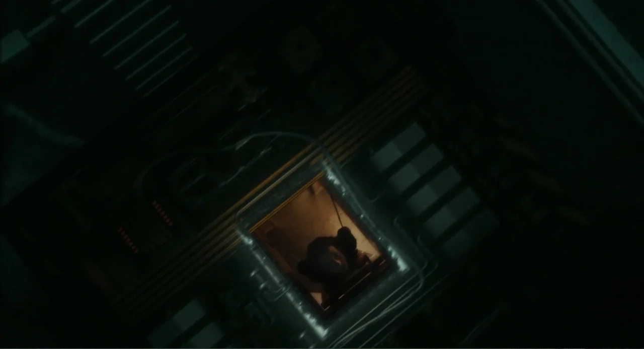 The Lift (2021) movie still: wide — A dark industrial metallic structure surrounds a square opening into a brightly lit space. A person looks up…