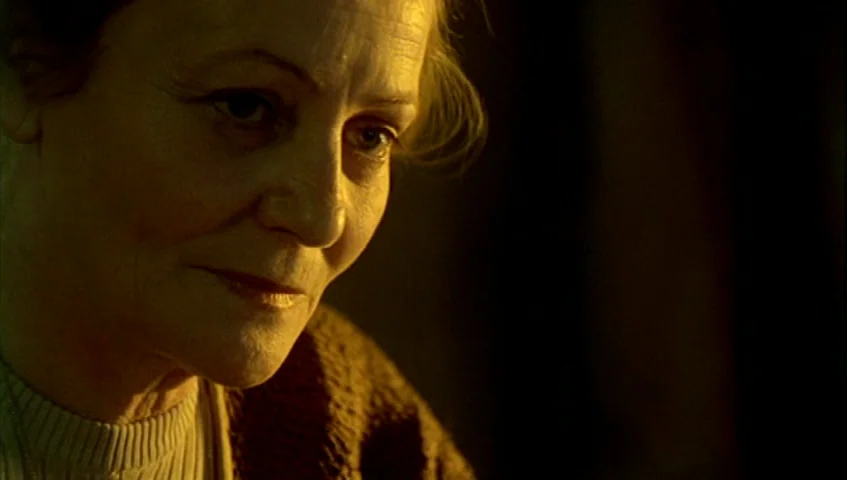 Almanac of Fall (1984) movie still: closeup — A dimly lit room with heavy shadows obscuring most of the background space. An elderly woman with fair…