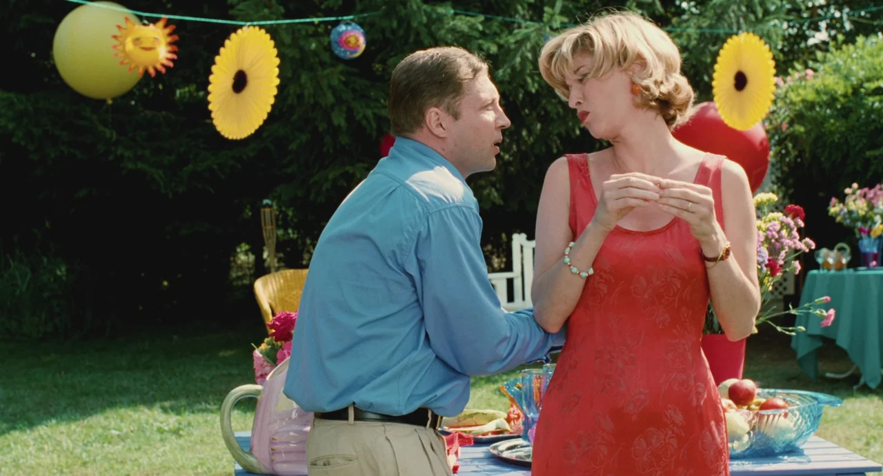 Ma Vie En Rose (1997) movie still: medium — A sunny backyard party features colorful paper decorations hanging between evergreen trees. A man in a…