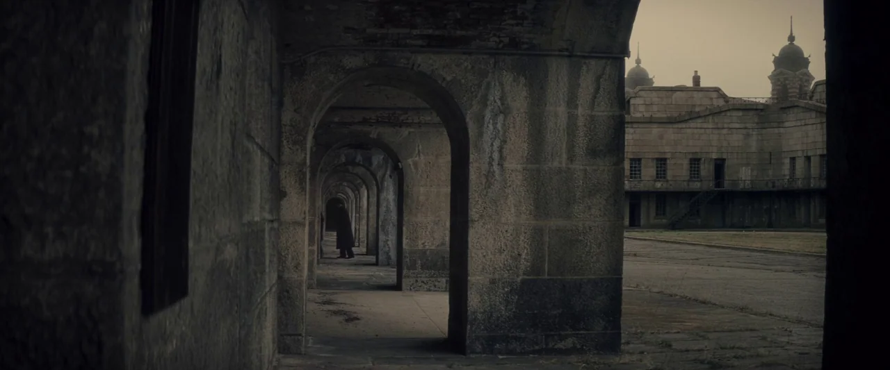 The Immigrant (2013) movie still: wide — A stone corridor with repeating archways overlooks a paved courtyard with historic brick buildings. A…