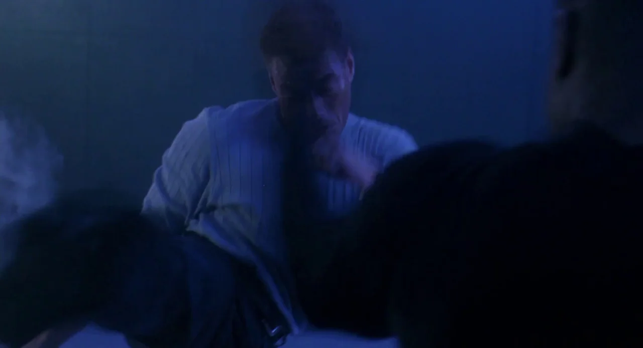 Universal Soldier: The Return (1999) movie still: medium — Two men engage in a physical fight inside a dark, blue-lit corridor. The primary subject…