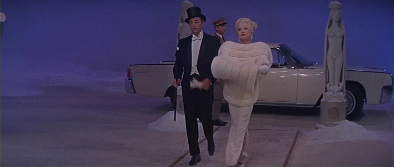 What A Way To Go! (1964) movie still: fullbody — A surreal studio set features stylized pillars and a purple, empty background. A man in formal…