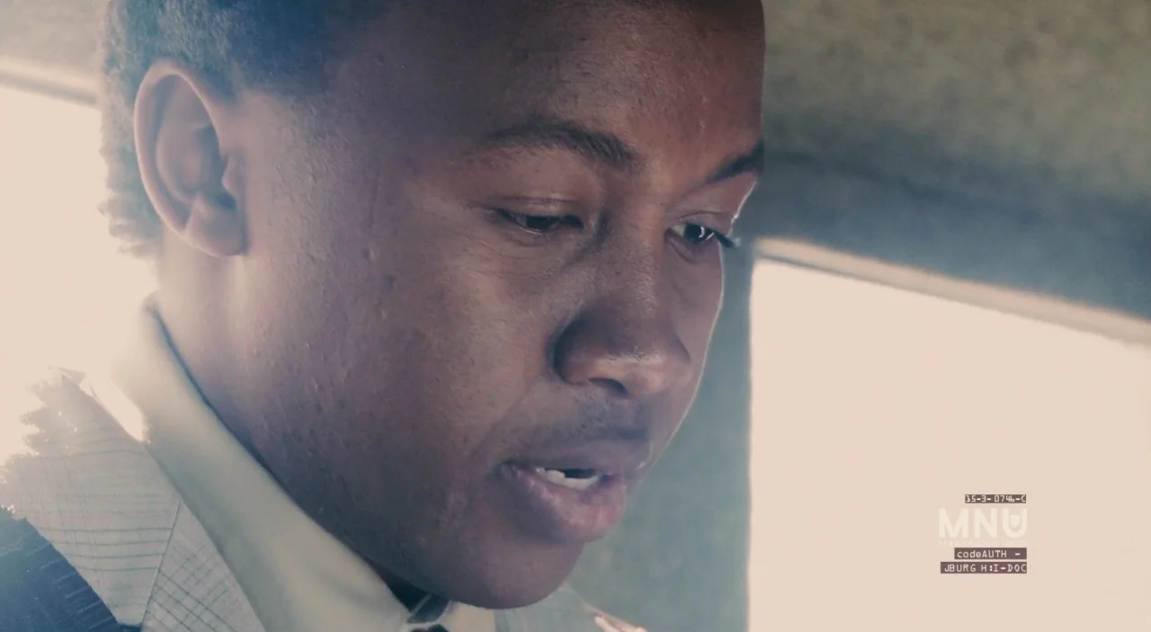 District 9 (2009) movie still: closeup — A close-up of a man inside a vehicle with bright light through the windows. The man looks down while…