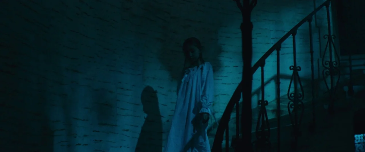 The Mad Hatter (2021) movie still: medium — A dimly lit staircase landing features a textured wall and wrought iron railings. A young child in a…