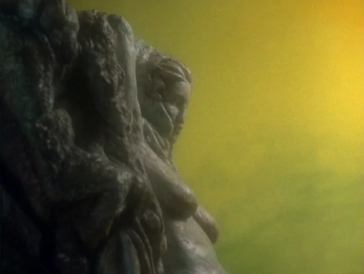 Twilight of the Ice Nymphs (1997) movie still: closeup — A stone statue of a female figure stands partially obscured by thick yellow haze. The…