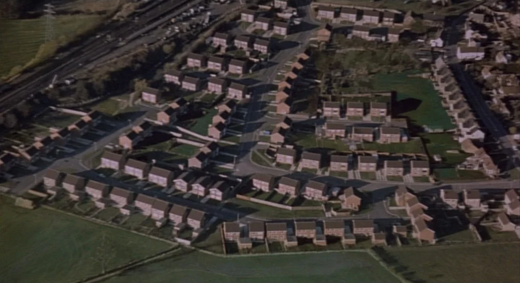 Time Bandits (1981) movie still: establishing — An aerial view of a dense residential suburban neighborhood with rows of identical houses. Winding…