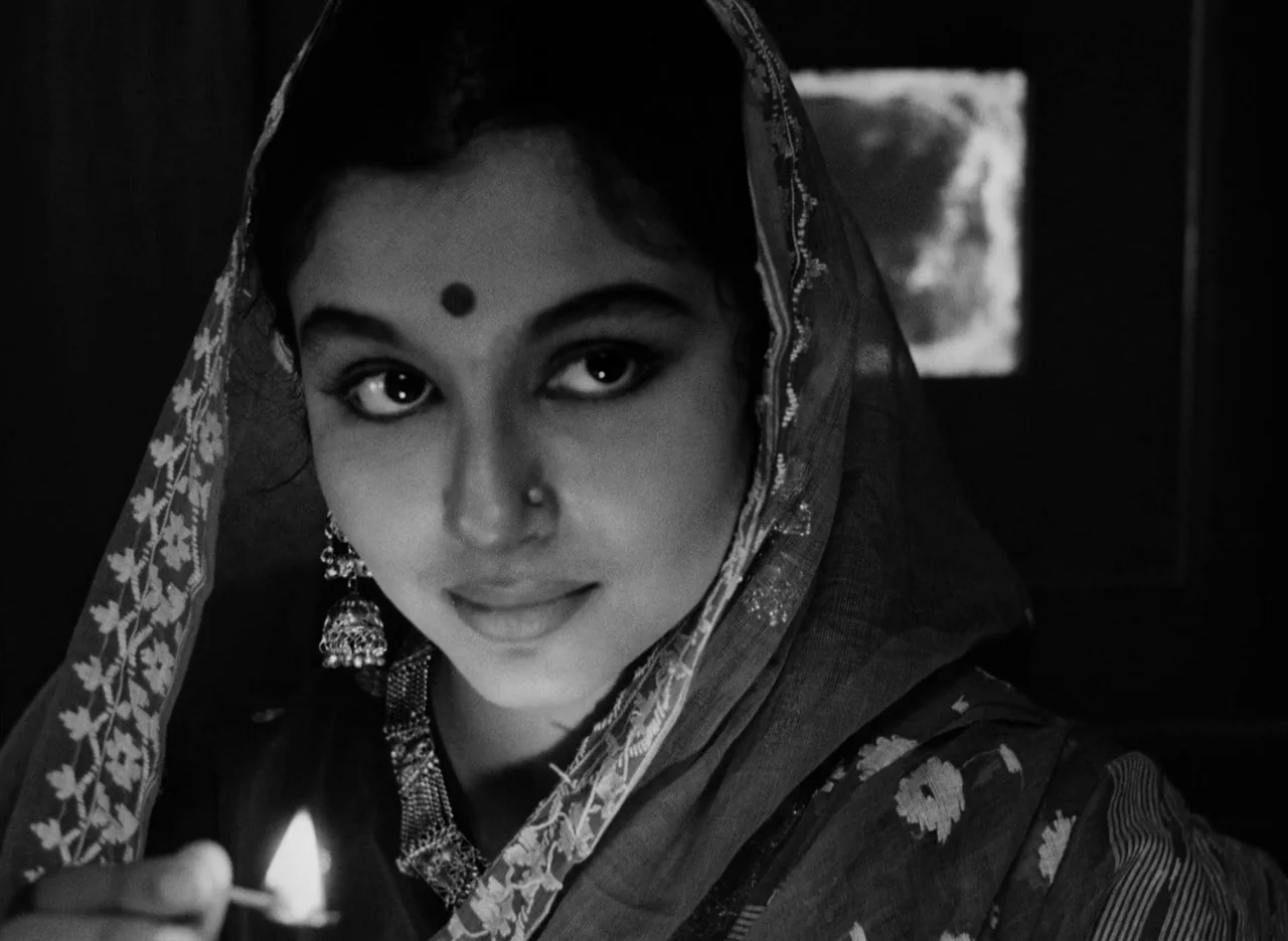 Apur Sansar (1959) movie still: closeup — A dark indoor space is illuminated by the flickering light of a small match. A woman with traditional…