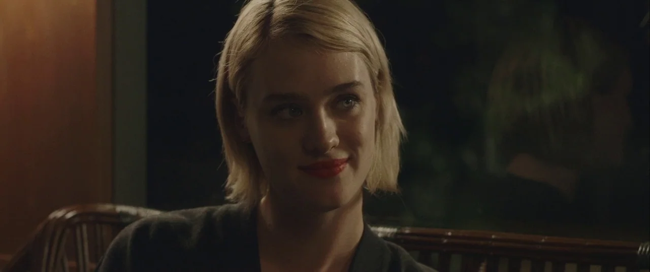 Always Shine (2016) movie still: closeup — A dimly lit restaurant setting features a wooden slatted backrest behind a woman. The woman stares…