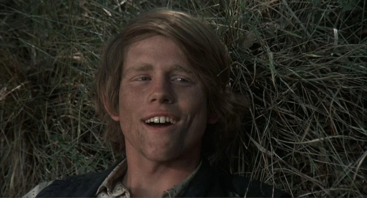 The Spikes Gang (1974) movie still: closeup — A patch of dry, tall grass serves as the background for a man's head. The man rests in the vegetation…