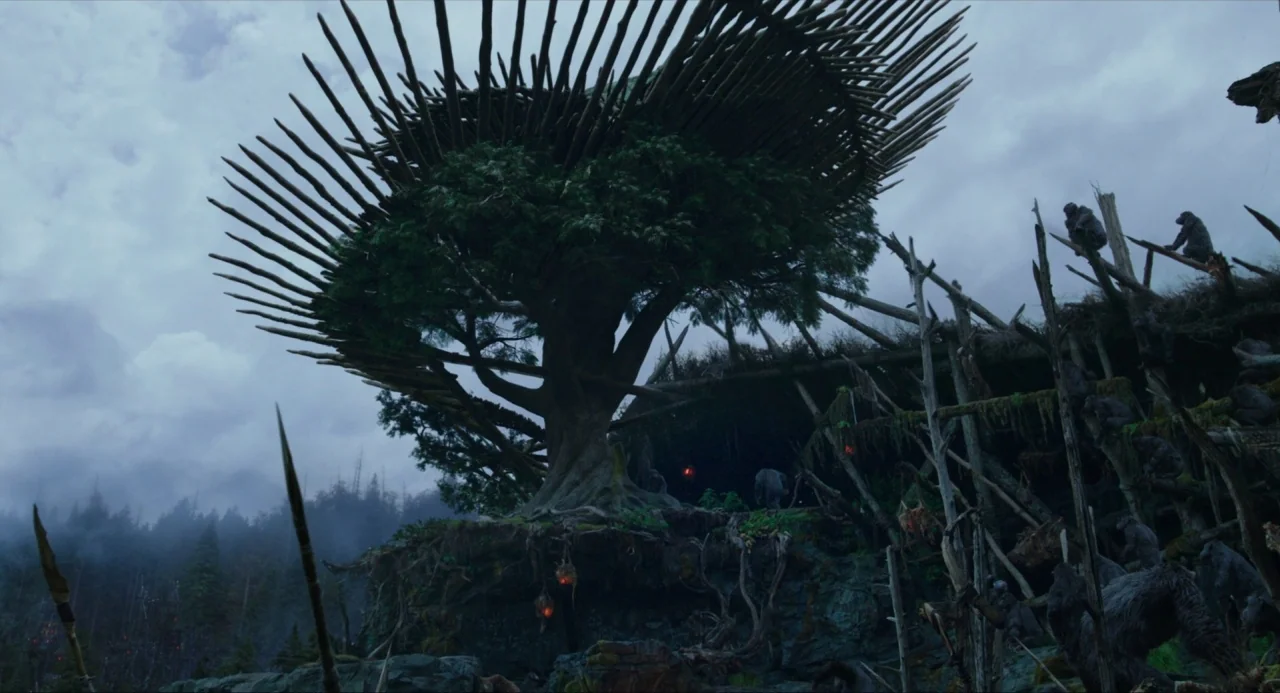Dawn of the Planet of the Apes (2014) movie still: establishing — A massive tree is fortified with a ring of sharp wooden poles in a forest. Several…