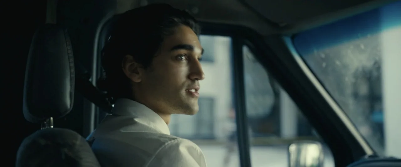 Dangerous Animals (2025) movie still: medium — The interior of a vehicle cabin is shown with a blurred urban environment outside. A young man…