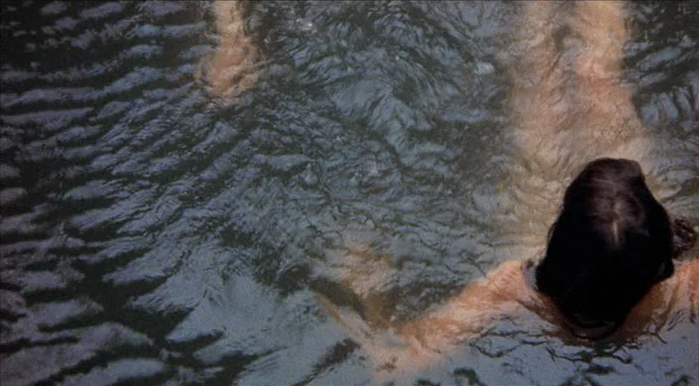 Easy Rider (1969) movie still: medium — A body of dark, rippling water fills the frame from a top-down perspective. A person swims near the surface…