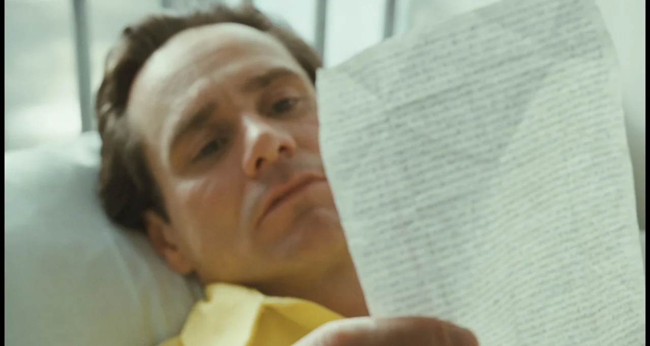 I Love You Phillip Morris (2010) movie still: closeup — A sterile room contains a hospital bed with a white pillow and railing. A man rests against…