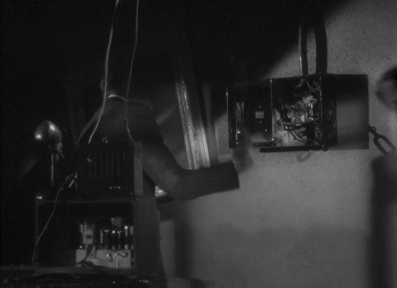 The Amazing Mr. X (1948) movie still: medium — A dark, spartan utility space features an exposed electrical panel mounted on concrete. A man in a…