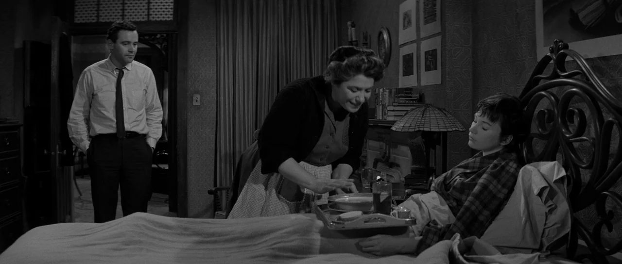 The Apartment (1960) movie still: medium — A 1950s bedroom contains a dark wood bed frame and walls with textured wallpaper. A woman places a tray…