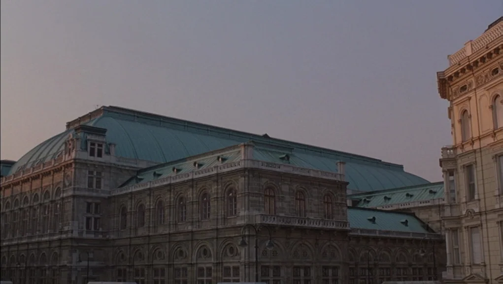 Before Sunrise (1995) movie still: establishing — A grand historic opera house with a green copper roof stands at twilight. The stone exterior…
