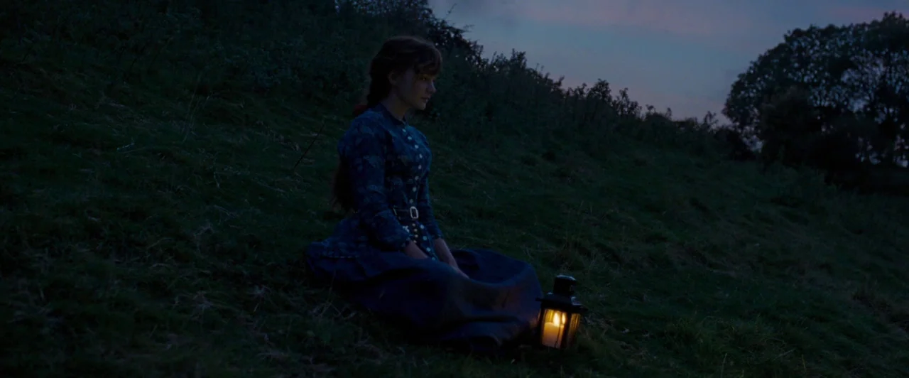 Far from the Madding Crowd (2015) movie still: medium — A woman sits alone on a dark, grassy hillside during the blue hour. She rests near a small,…