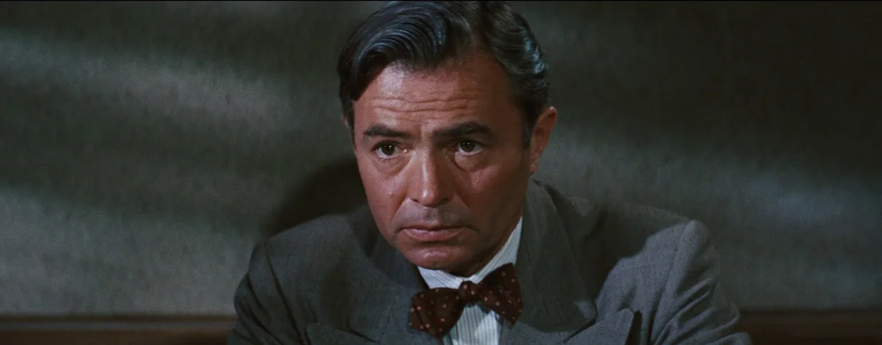 Bigger Than Life (1956) movie still: closeup — A man stands against a blurred, indistinct background in a dimly lit indoor space. He gazes straight…
