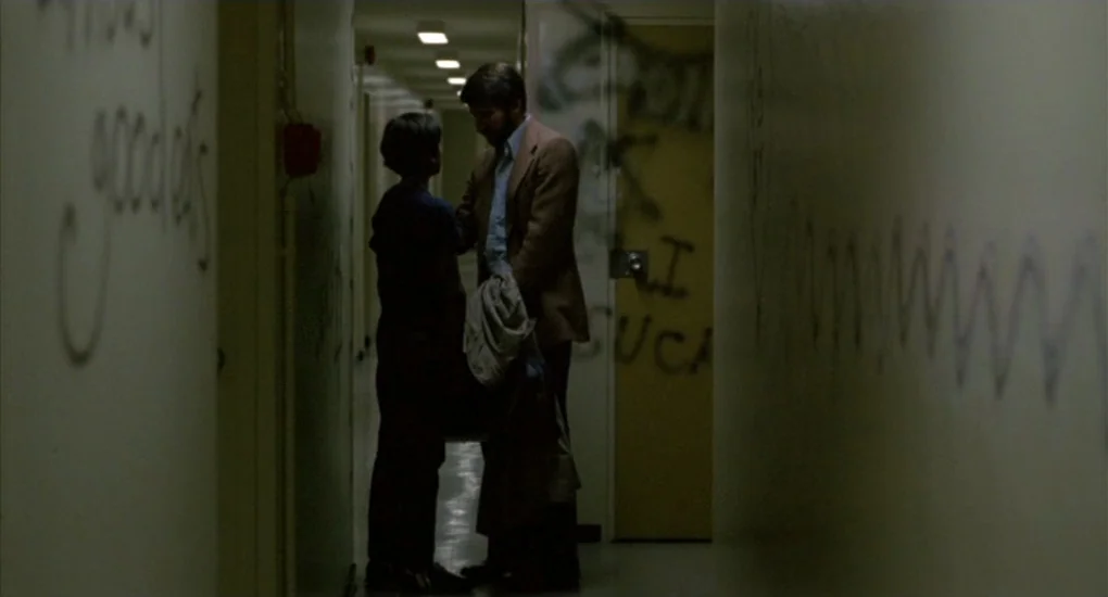The Killing Fields (1984) movie still: fullbody — A dark apartment hallway features pale walls covered in dark, hand-scrawled graffiti. A man and a…