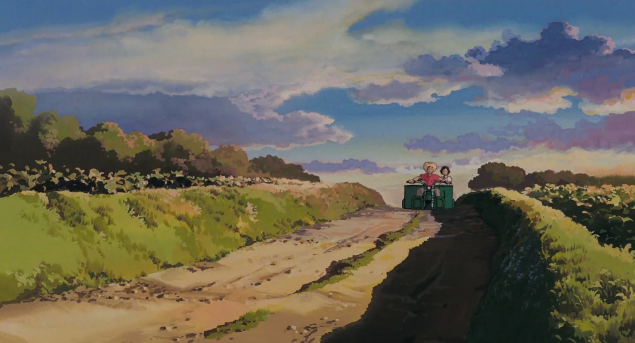 My Neighbour Totoro (1988) movie still: wide — A rural dirt path winds through lush green fields under a vibrant sunset sky. Two figures travel away…