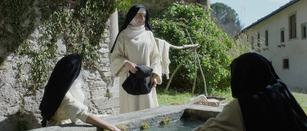 The Little Hours (2017) movie still: medium — An outdoor courtyard features an old stone basin near a weathered ivy-covered wall. Three nuns in…