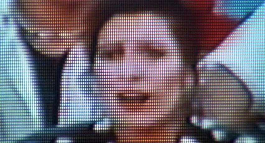 Matador (1986) movie still: closeup — A close-up view of a face rendered through a visible CRT monitor pixel grid. The screen displays a…