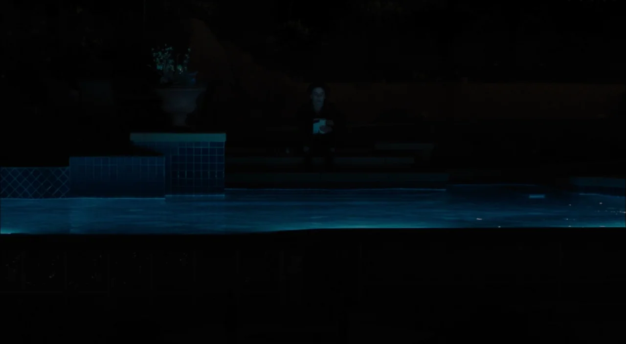 Lady Bird (2017) movie still: wide — A dark night setting beside a backyard pool with illuminated underwater tiles. A lone person sits on the pool…
